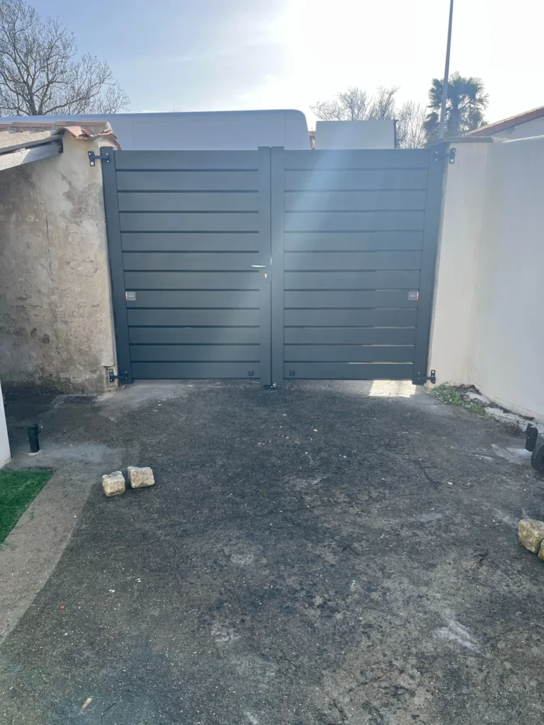 Portail battant en aluminium gris anthracite à lames pleines fermé entre deux piliers, vu de la cour, Salles-sur-Mer